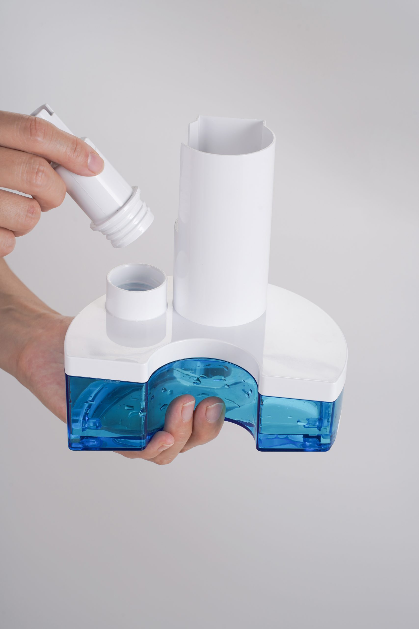 Hands connect/assemble a white humidifier with a blue water tank, focusing on the cylindrical top piece and cap being twisted on.